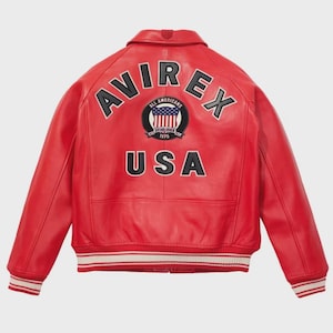 May include: A red leather jacket with the word "AVIREX" arched across the shoulders in black and white lettering. Below, the word "USA" is displayed. A circular patch with the American flag is centered between the words. The jacket has a collar and striped cuffs.
