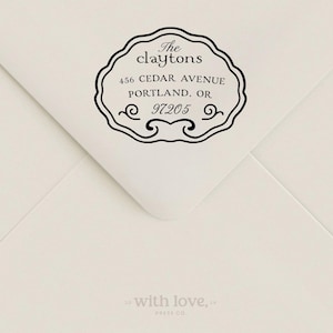 May include: A black ink address stamp impression on a cream-colored envelope. The stamp features a decorative scalloped border and reads: The claytons, 456 CEDAR AVENUE, PORTLAND, OR, 97205. The text with love, PRESS CO. is printed at the bottom.