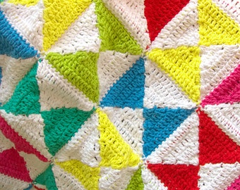 Puede incluir: Una manta de crochet colorida con un patrón geométrico de triángulos en tonos de rojo, amarillo, verde, azul y blanco.