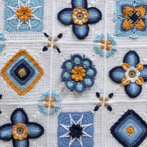 May include: A white crocheted blanket with a repeating pattern of blue and yellow flowers. The blanket is made up of squares with different designs, including a star, a diamond, and a flower.