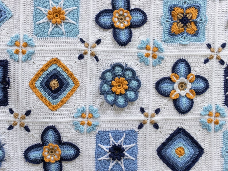 May include: A white crocheted blanket with a repeating pattern of blue and yellow flowers. The blanket is made up of squares with different designs, including a star, a diamond, and a flower.