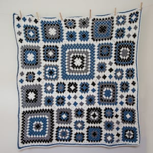 May include: A white crocheted blanket with a geometric pattern in shades of blue and black.