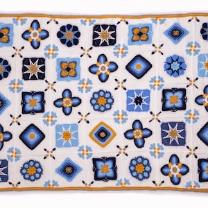 May include: A crocheted blanket with a white background and a pattern of blue and yellow squares. The squares are arranged in a grid pattern and each square has a different design.