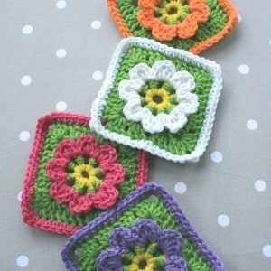 May include: Four crocheted granny squares with different colored flowers in the center. The squares are green, white, pink, and purple.