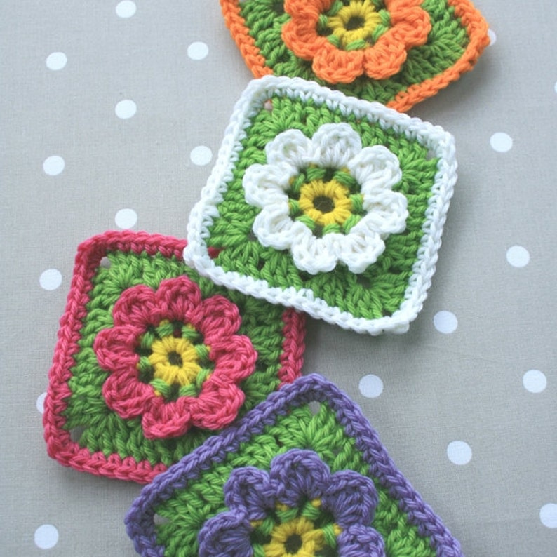 May include: Four crocheted granny squares with different colored flowers in the center. The squares are green, white, pink, and purple.