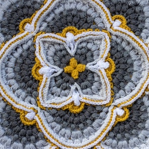 Peut inclure: Un carré crocheté avec un motif central de quatre fleurs jaunes et blanches entourées d'une bordure de fil jaune et blanc.