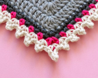May include: Close-up of a crocheted corner with a gray center, a pink border, and a white scalloped edge.