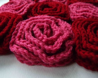 May include: Close-up of several handmade crochet roses in shades of red and pink. The roses are tightly wound, showcasing the texture of the yarn. The arrangement suggests a floral theme, possibly for crafts or home decor.