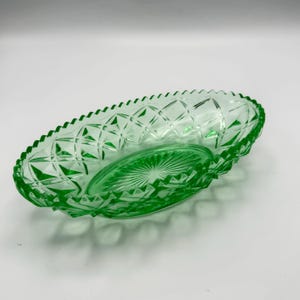 May include: A green glass oval dish with a diamond pattern and a scalloped edge. The dish has a smaller, oval insert with a sunburst design. The glass is a vibrant, transparent green.