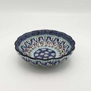 May include: A ceramic bowl with a scalloped rim, featuring a detailed blue and white floral pattern. The bowl's interior showcases a central design of blue floral motifs, with a dark blue rim and a light blue and white pattern around the edges.