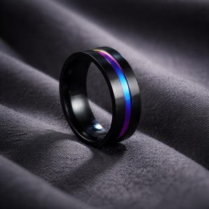 May include: A black ring with a vibrant, iridescent stripe of blue, purple, and yellow. The ring has a polished finish and a sleek, modern design. This piece of jewelry is suitable for everyday wear.
