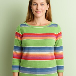 May include: A green sweater with horizontal stripes in various colors, including red, orange, blue, and purple. The sweater has a boat neck and three-quarter sleeves. The person is wearing blue jeans.