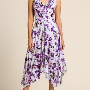 May include: A sleeveless, white dress with a purple floral pattern. The dress features a V-neckline, a fitted waist, and an asymmetrical hemline. The model is wearing brown high-heeled sandals.
