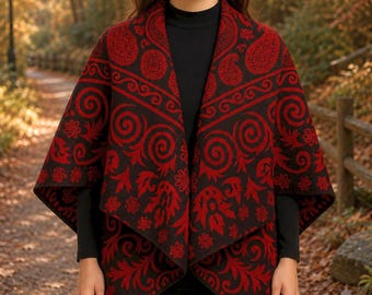 May include: A black and red open-front poncho featuring a repeating pattern of paisley motifs, swirling scrolls, and floral elements. The garment has a draped silhouette with an asymmetrical hemline and is worn over a solid black long-sleeve top.