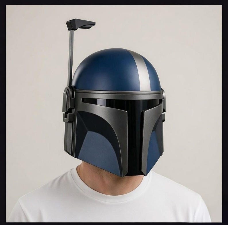 May include: A Mandalorian helmet in shades of blue and gray, with a silver stripe down the center of the dome. The helmet has a T-shaped visor and a vertical antenna-like structure extending from the top.