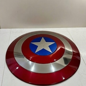 May include: A red, silver, and blue shield with a star emblem. The shield is round with a glossy finish. The outer ring is red, followed by a silver band, and a blue center with a white star.
