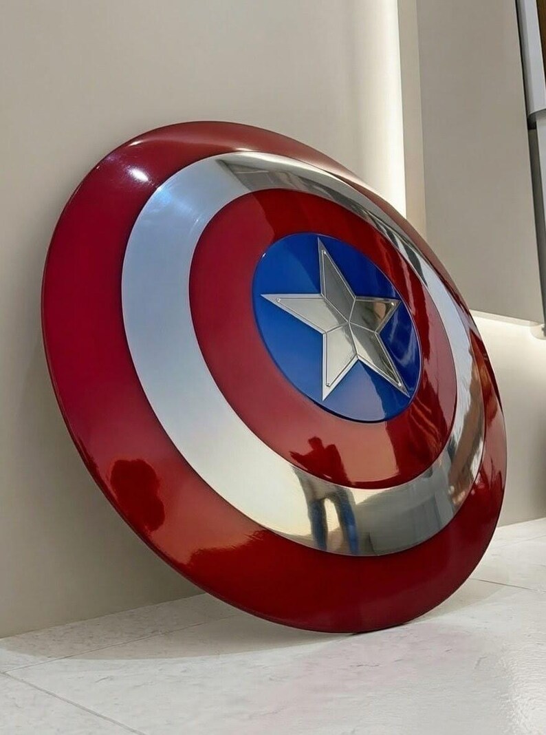 May include: A glossy, red, white, and blue shield with a silver star in the center. The shield has concentric circles of red, silver, and blue. A classic superhero accessory.