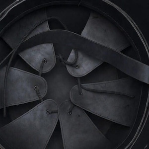 May include: Close-up of the interior of a black helmet. The helmet's interior features a series of dark leather or fabric panels, secured with laces, radiating from the center. A black strap crosses the interior, adding structural support.