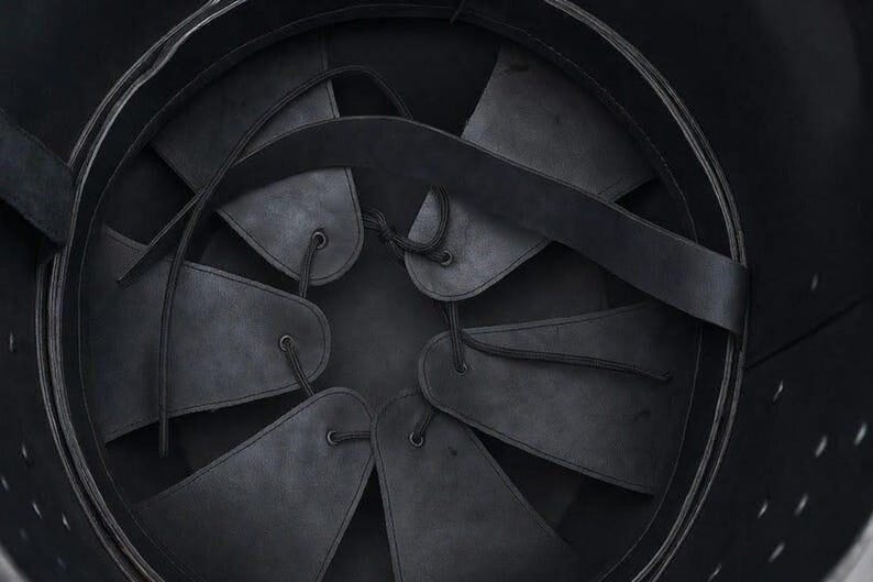 May include: Close-up of the interior of a black helmet. The helmet's interior features a series of dark leather or fabric panels, secured with laces, radiating from the center. A black strap crosses the interior, adding structural support.