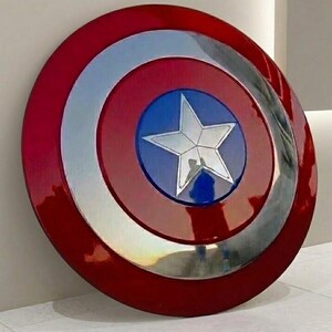 May include: A round shield with a red, silver, and blue color scheme. The shield features a central blue circle with a silver star, surrounded by silver and red concentric rings. The shield is a replica of Captain America's shield.