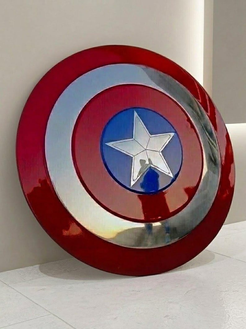 May include: A round shield with a red, silver, and blue color scheme. The shield features a central blue circle with a silver star, surrounded by silver and red concentric rings. The shield is a replica of Captain America's shield.