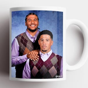 Puede incluir: Una taza de cerámica blanca con una fotografía impresa de dos personas con camisas abotonadas de color morado claro y chalecos de punto con rombos. El fondo es azul texturizado. El texto "HIGHLIGHT SPORTS" aparece en la esquina inferior.