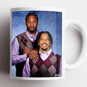 May include: A white ceramic mug featuring a printed photograph of two individuals wearing light purple dress shirts and argyle sweater vests. The background is a textured blue. The text HIGHLIGHT SPORTS is printed in the bottom right corner.