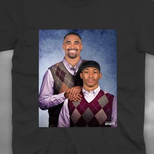 Puede incluir: Una camiseta negra de manga corta con un estampado gráfico central de dos personas con camisas de vestir de color morado claro y chalecos de rombos. El gráfico incluye el texto HIGHLIGHT SPORTS en la esquina inferior derecha.