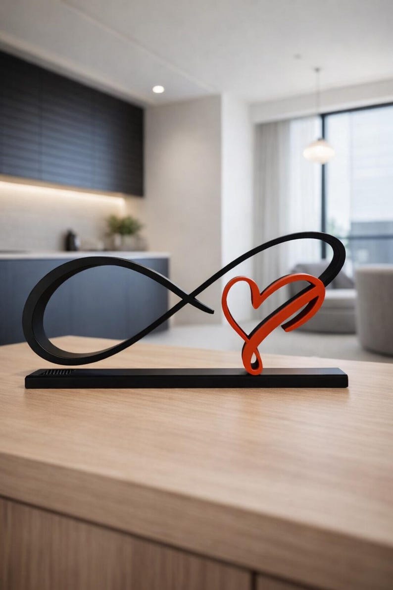 May include: A black metal sculpture featuring an infinity symbol intertwined with a red heart. The piece is mounted on a black base. It is displayed on a light wood table in a modern living room setting.