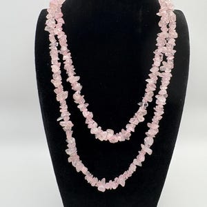 May include: A double-strand necklace featuring numerous small, irregular, translucent pale pink rose quartz chips strung together. The necklace displays a layered appearance with the light pink stones creating a textured, organic look throughout.