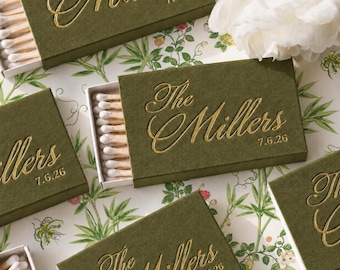 May include: Olive green matchboxes featuring gold foil embossed text that reads The Millers and the date 7.6.26. Each rectangular box is partially open, revealing a row of wooden matches with white tips arranged inside the sliding tray.