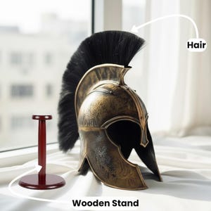 Puede incluir: Un casco espartano de color bronce con una pluma negra, exhibido en un soporte de madera rojo oscuro. El casco tiene detalles intrincados y una apariencia desgastada. El soporte es redondo en la base y en la parte superior, con un soporte vertical.