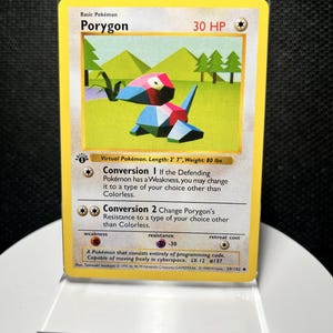 May include: A Porygon trading card featuring a geometric, multi-colored creature in a green landscape. The card displays 30 HP, the text Conversion 1 and Conversion 2, and a first edition stamp. It is encased in a clear protective plastic sleeve.
