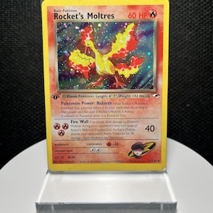 May include: A Rocket's Moltres holographic trading card featuring a yellow and orange bird illustration, 60 HP, and the text 'Flame Pokémon. Length: 6' 7", Weight: 132 lbs.' The card displays the Pokémon Power Rebirth and the Fire Wall attack.