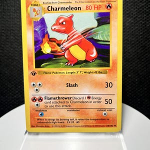 May include: A 1999 Wizards of the Coast Charmeleon trading card, Stage 1, 80 HP, featuring a red fire-type creature illustration. The card displays the attacks Slash and Flamethrower, with text detailing its length of 3' 7" and weight of 42 lbs.