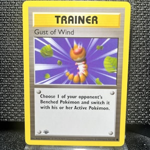 May include: A Pokémon Trainer card titled "Gust of Wind." The card has a yellow border and features an illustration of a caterpillar-like creature with green leaves. Text on the card describes the card's function in the game.