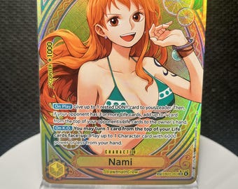 May include: A holographic One Piece trading card featuring the character Nami with orange hair, wearing a green and white bikini top. The card displays a power level of 6000, a cost of 5, and detailed game text in English against a gold background.