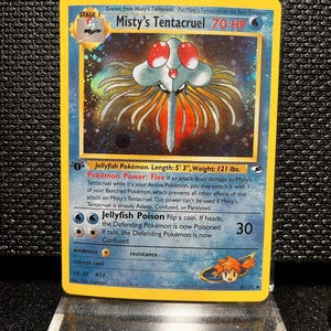 May include: A holographic Misty's Tentacruel Pokémon card. The card features a blue and yellow border with the text "Misty's Tentacruel" and "70 HP". The illustration depicts a jellyfish-like creature with red eyes and orange tentacles. The card is 5' 3" long and weighs 121 lbs.