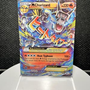 May include: A MCharizard EX trading card with 220 HP, featuring a dynamic illustration of a dragon-like creature surrounded by blue and yellow energy effects. The card displays the Heat Typhoon attack, Japanese text, and standard game rules.