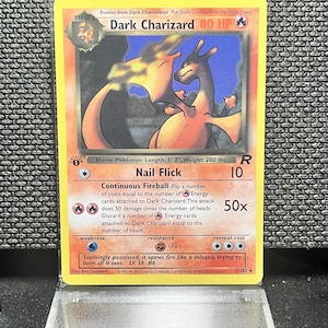 May include: A Dark Charizard trading card featuring a fire-breathing dragon illustration, 80 HP, and the Nail Flick attack. The card displays the text 'Flame Pokémon. Length: 5' 7", Weight: 200 lbs.' and is encased in a clear protective plastic display stand.