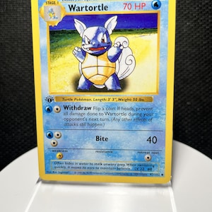 May include: A Wartortle trading card in a clear protective sleeve. The card features a blue turtle character, 70 HP, and the attacks Withdraw and Bite. Text includes 'Turtle Pokémon. Length: 3' 3", Weight: 50 lbs.' and copyright information.