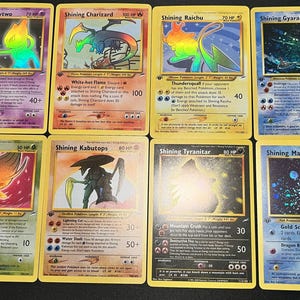 Puede incluir: Una colección de ocho cartas coleccionables de Pokémon, cada una con un personaje diferente con un diseño holográfico. Las cartas tienen un borde amarillo e incluyen personajes como Mewtwo, Charizard y Gyarados.
