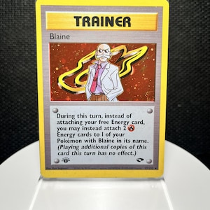 May include: A Blaine Trainer trading card featuring a holographic illustration of a man with a white mustache and glasses wearing a white lab coat and pink tie. The card includes text describing game mechanics and a first edition stamp symbol.