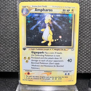 May include: A yellow Ampharos Pokémon card. The card features a yellow and white creature with a lightning bolt design. The card has text that reads "Ampharos" and "Gigaspark". The card is in a protective sleeve.