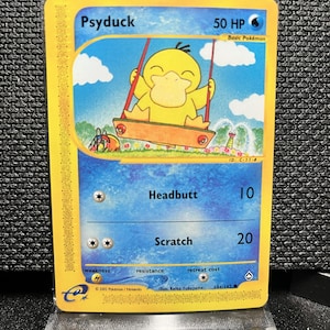 Puede incluir: Una carta coleccionable de Pokémon con Psyduck, un Pokémon amarillo con forma de pato, en un columpio. La carta tiene un borde amarillo y un fondo azul con el texto "Psyduck" y "50 HP". La carta también incluye el texto "Headbutt" y "Scratch".