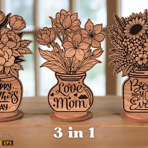 Op de afbeelding: Drie houten bloemstukken met lasergesneden ontwerpen. Elk arrangement heeft een ander bloemtype in een vaasvormige houder. De vazen hebben de tekst "Happy Mother's Day", "Love Mom" en "Best Mom Ever".