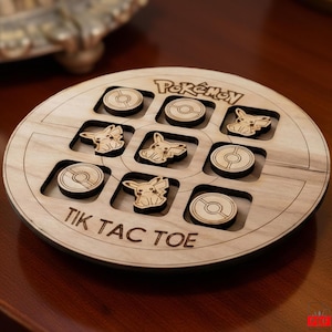 Peut inclure: Jeu de Tic-Tac-Toe en bois avec des personnages Pokémon et des jetons Poké Ball. Le plateau de jeu circulaire présente des motifs découpés au laser et le mot "Pokémon" en haut. L'expression "TIK TAC TOE" est en bas.