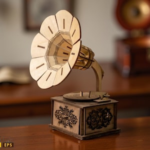 May include: A wooden model of a vintage gramophone. The gramophone features a large, flared horn and a decorative wooden box base. The model is made of light-colored wood and has intricate cut-out details. The gramophone is displayed on a dark wooden surface.