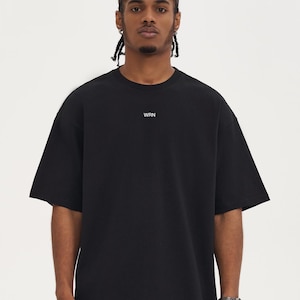 May include: Black short-sleeved t-shirt with the letters "WRN" printed in white on the chest. The shirt has a relaxed fit and a crew neck. The model is wearing a silver watch.