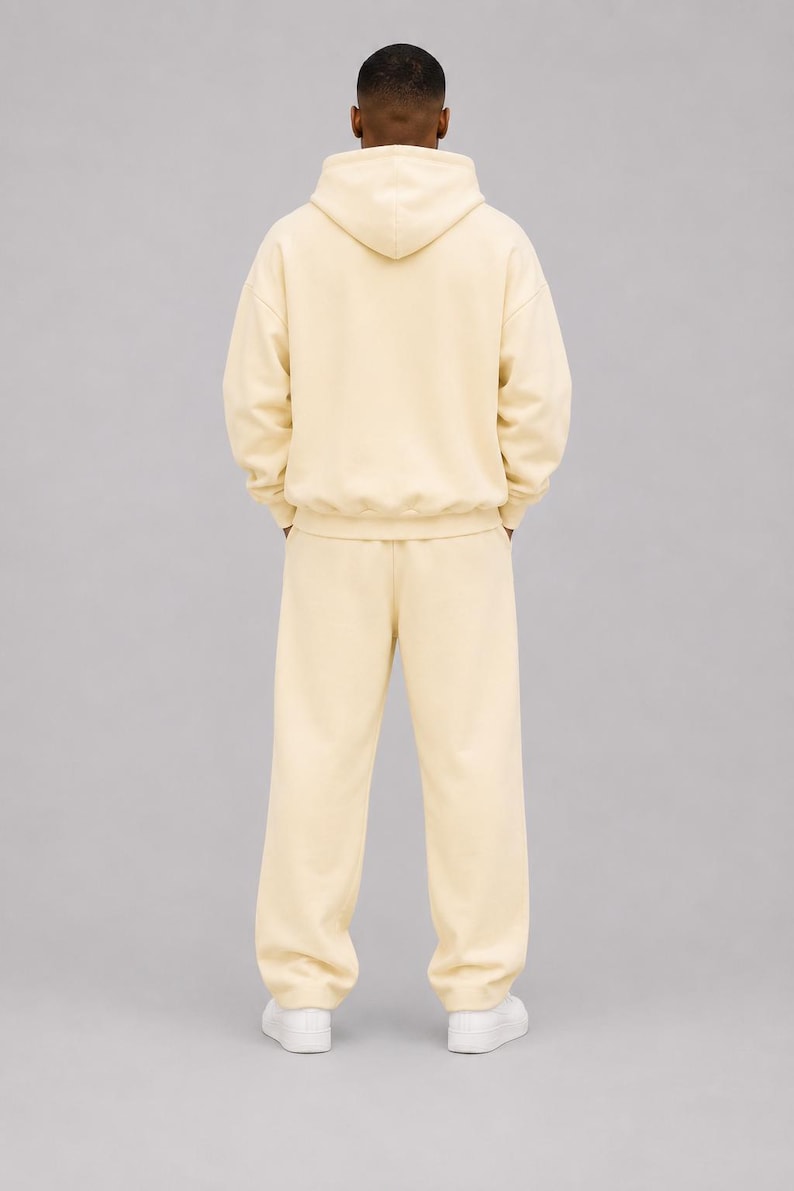 May include: A cream-coloured matching set consisting of a long-sleeved hooded sweatshirt and loose-fitting sweatpants. The hoodie features a hood and ribbed cuffs, while the sweatpants have a straight-leg cut. The outfit is paired with white trainers.